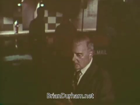 The still from the 1960s Boy Scouts PSA features a serious-looking man in a suit, likely addressing a group of Boy Scouts or demonstrating a safety message. The setting appears to be indoors, with soft lighting and a background suggestive of a community space. The overall tone reflects a focus on responsibility and education.