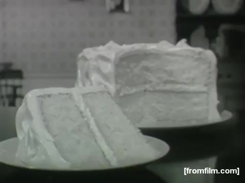 The still features a beautifully frosted cake and a slice of the same cake on a plate. The cake has a light, fluffy texture, and is covered in white icing, emphasizing its classic French vanilla flavor. The background suggests a cozy kitchen setting, typical of early 1960s home cooking advertisements.
