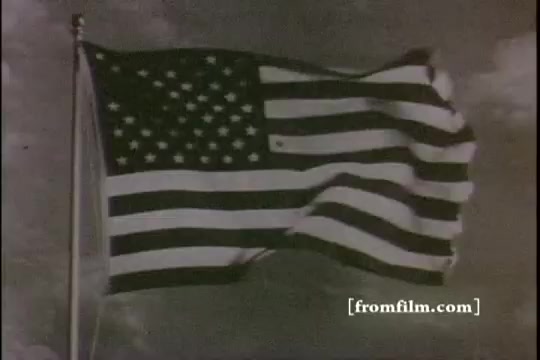 The still depicts the American flag waving in the wind against a cloudy sky. The image is in black and white, characteristic of 16mm film prints, conveying a nostalgic and historical feel, likely underscoring themes of patriotism and national identity in the context of the film 'Great Moments in History - Thomas Edison - Army Recruiting.'