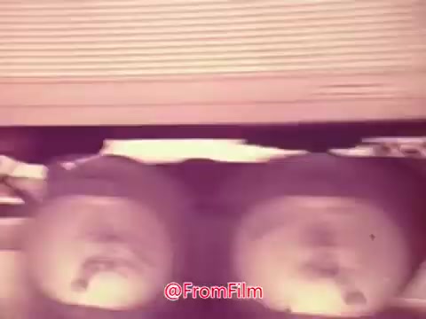 The still from the 1976 movie trailer 'Drive-In' features a close-up of wheels, likely from a vehicle in motion. The image conveys a sense of movement and anticipation, typical of the dynamic style used in trailers of that era. The color palette appears faded, evoking a vintage aesthetic consistent with 16mm film. Overall, it captures the essence of classic drive-in cinema culture.