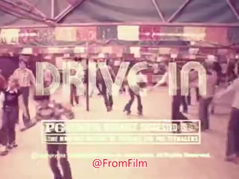 The still from the trailer for 'Drive-In' (1976) features a bustling scene filled with teenagers enjoying themselves in a lively atmosphere, presumably at a drive-in movie theater. The title 'DRIVE IN' is prominently displayed, along with a PG rating. The vibrant energy suggests a fun, youthful film capturing the essence of the era. The background hints at the outdoor setting, with colorful banners and people milling about. Overall, it invokes a sense of nostalgia for drive-in culture.