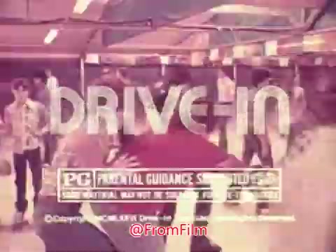 The still from the 1976 trailer for 'Drive-In' features the title prominently displayed in bold, stylized lettering. Below the title, there's a 'PG' rating indicating parental guidance is suggested. The image portrays a scene with several people, likely in a social or entertainment setting typical of a drive-in atmosphere. The overall aesthetic reflects the retro style of the 1970s, giving a nostalgic glimpse into that era's youth culture and leisure activities.