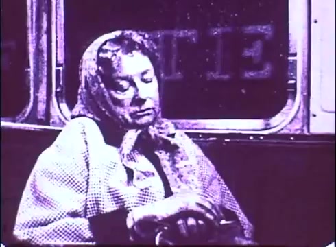 The still from the trailer of 'The Laughing Policeman' depicts an elderly woman with a contemplative expression, sitting in a dimly lit subway or bus setting. She is wearing a patterned scarf and a textured coat, giving a sense of weariness. The background features blurred, indistinct text, contributing to the overall atmosphere of urban introspection. The monochromatic treatment lends a vintage aesthetic typical of a 16mm print.