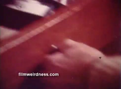 The still from the 1970s Ben Gay commercial features a close-up of a hand interacting with a piece of furniture, suggesting warmth and comfort. The lighting is soft, creating a nostalgic and inviting atmosphere typical of advertisements from that era. The focus is on the hand's action, emphasizing the personal touch associated with the product.