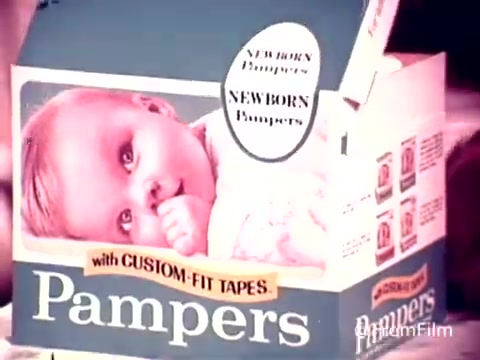 The still features a vintage Pampers diaper box from the 1970s, prominently displaying a cheerful baby sucking on their thumb. The package is labeled 'NEWBORN Pampers' and highlights 'with CUSTOM-FIT TAPES.' The design reflects the aesthetic of that era, showcasing bright colors and playful typography. The overall vibe evokes nostalgia, representing a time when diaper commercials focused on comfort and care for infants.