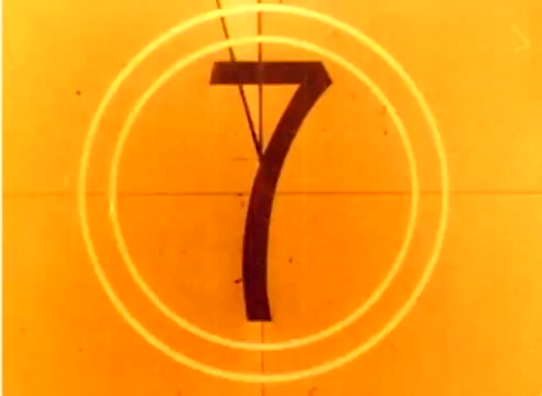 The still features a close-up of a countdown marker in an orange hue, displaying the number '7' within concentric circles. This is indicative of a 16mm silent film format, typical for production eras like that of the 1977 Kodak sales film featuring Michael Landon and Dick Van Dyke. The overall aesthetic conveys a nostalgic feel, commonly associated with vintage marketing materials from that time, leading into the Christmas season.