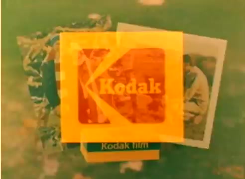 The still features the Kodak logo prominently in orange against a blurred background, accompanied by images of film-related materials. It suggests a promotional context, likely showcasing Kodak's offerings in preparation for the 1977 Christmas season, as highlighted by the connection to Michael Landon and Dick Van Dyke. The overall aesthetic reflects a vintage, nostalgic feel typical of the era.