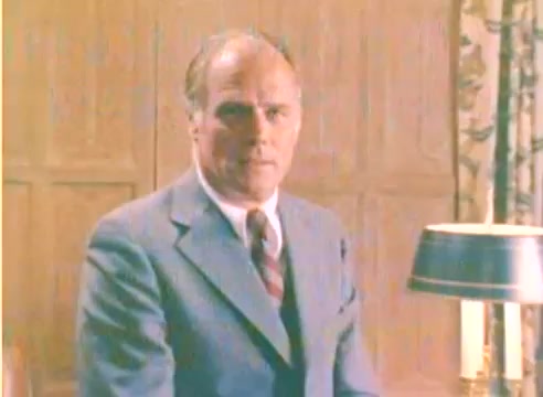 The still features a well-dressed man, likely portraying a serious demeanor, sitting in a room with wood-paneled walls. A table lamp is positioned in front of him, casting a warm glow. The overall color tone suggests a vintage aesthetic, typical of a 1970s film. The absence of sound emphasizes the visual storytelling in this promotional piece for Kodak leading into the Christmas season.