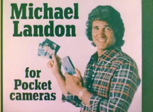 The still features Michael Landon promoting Kodak's pocket cameras. He is smiling and holding two camera models, showcasing their compact design. The background includes bold text stating “Michael Landon for Pocket cameras.” The overall aesthetic reflects a colorful, retro style typical of 1970s advertising, aiming to capture attention during the Christmas season.
