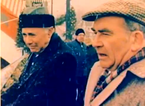 The still from the 'Kodak 1977 Sales Film' features two men, presumably Michael Landon and Dick Van Dyke, standing outdoors in a snowy setting. They are dressed in winter attire, with one wearing a fur hat and the other a checked cap. The scene conveys a cold atmosphere, fitting for the holiday season theme of the film. The image is vibrant, typical of color negatives from that era, and captures a moment of contemplation or conversation between the two figures amid a wintry backdrop.
