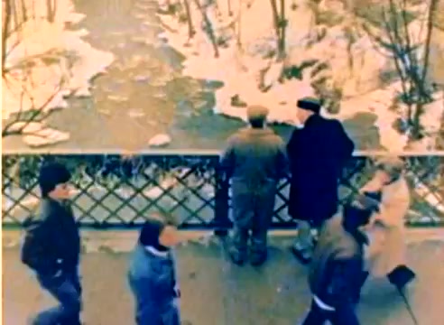 The still from the 'Kodak 1977 Sales Film' features two men standing by a bridge, looking down at a partially frozen river. They are flanked by passersby, suggesting a busy scene. The color palette is warm and muted, reflective of the film's nostalgic vibe as it promotes Kodak's products for the upcoming Christmas season. The setting indicates a winter atmosphere, enhancing the seasonal theme of the film.