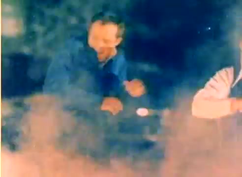 The still from the 'Kodak 1977 Sales Film' features Michael Landon and Dick Van Dyke in a playful, dynamic scene, likely showcasing the spirit of the Christmas season. The footage is taken from a 16mm silent negative, emphasizing the nostalgic feel of the era. The colors appear warm and slightly faded, typical of the film stock from that time. There is an atmosphere of joy and camaraderie between the two actors, suggesting a lighthearted promotional theme.