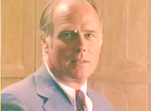 The still from the 'Kodak 1977 Sales Film' features a man in a tailored suit with a serious expression, set against a lightly colored wooden backdrop. The image reflects the visual style of the late 1970s, with a soft focus and warm tones, characteristic of Kodak's promotional materials. This silent workprint captures a moment from a film likely intended to showcase Kodak's offerings for the Christmas season.