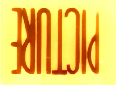 The still from the 'Kodak 1977 Sales Film' features the word 'PICTURE' rendered in a bold, stylized font against a bright yellow background. The colors are warm, likely characteristic of the film stock used, and the overall look evokes the nostalgic aesthetic of the late 1970s. The text appears to be inverted, suggesting a playful or experimental take typical of silent film techniques. This emphasizes the promotional nature of the film during the Christmas season, highlighting Kodak’s focus on capturing vivid moments.