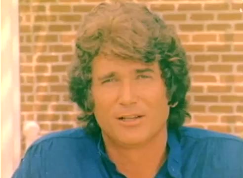 The still features a young Michael Landon, appearing casual, wearing a blue shirt. He's set against a backdrop of a brick wall. The image is from a 16mm silent color negative, part of a Kodak sales film promoting the 1977 Christmas season. The overall tone is warm and nostalgic, characteristic of that era's visual style.