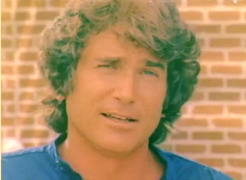 The still captures a young Michael Landon, sporting his characteristic curly hair and wearing a blue shirt. The background features a brick wall, contributing to a nostalgic ambiance fitting for a 1977 sales film. This silent color negative likely showcases Landon's charisma as part of the promotional material for Kodak leading into the Christmas season.