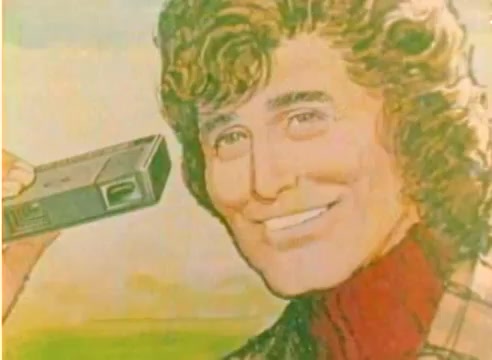 The still from the 'Kodak 1977 Sales Film' features a stylized image of a man with curly hair, smiling as he holds a small video camera. The background suggests a pastoral setting, likely reflecting the holiday spirit of the 1977 Christmas season. The presentation aligns with the promotional tone typical of Kodak sales materials, showcasing their products for home video storytelling.