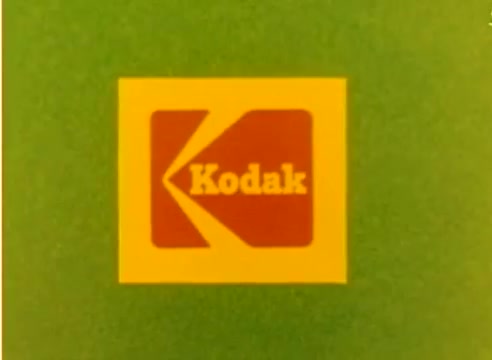The still features the Kodak logo prominently displayed in red and yellow on a green background. This is from a 16mm silent color negative of a sales film, likely intended to promote Kodak products during the lead-up to the 1977 Christmas season. The context suggests a focus on the nostalgic and festive spirit associated with the holiday and the brand.