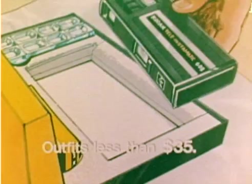 The still from the 'Kodak 1977 Sales Film' features a hand placing a cassette tape into an empty box, likely representing a product offering. The text 'Outfits less than $35' is displayed prominently, suggesting a promotional message for affordable products. The overall tone is cheerful and festive, aligning with the Christmas season. The image is part of a silent color negative, emphasizing visual appeal without dialogue.