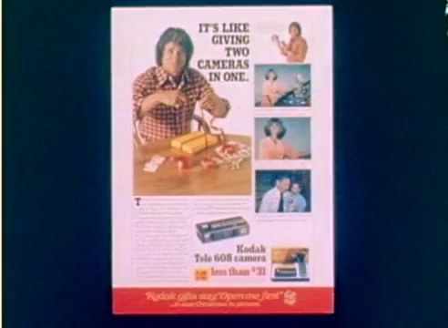 The still features a colorful advertisement promoting the Kodak Tele 608 camera, highlighting its dual functionality. Central to the image is an enthusiastic male presenter, possibly Michael Landon, holding a camera and engaging with the audience. Surrounding him are visuals showcasing the camera's features and different uses, including images of various subjects being photographed. The text emphasizes the value of the camera, stating, 'It's like giving two cameras in one,' and mentions its affordability at less than $33. The overall tone is festive, aligning with the promotion for the 1977 Christmas season.