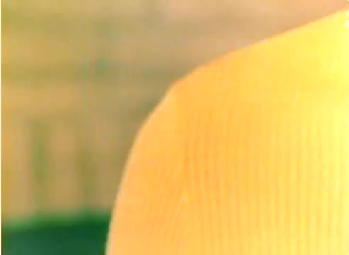The still from the 'Kodak 1977 Sales Film - Michael Landon/Dick Van Dyke' features a close-up of a yellow knitted fabric against a blurred background, possibly hinting at a festive theme. The emphasis on color and texture aligns with the promotional context of the film aimed at the Christmas season. The overall composition suggests a warm, inviting atmosphere characteristic of holiday communications.