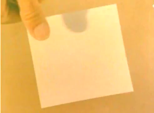 The still from the 'Kodak 1977 Sales Film' features a close-up of a hand holding a blank square piece of paper against a neutral background. The warm tones suggest a nostalgic feel, typical of vintage film. This seemingly simple composition may serve as a visual device to emphasize ideas related to creativity or potential in the context of Kodak's promotional message for the Christmas season.