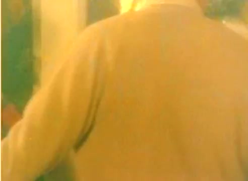 The still from the 'Kodak 1977 Sales Film' features a figure with their back turned, wearing a light-colored sweater. The background is softly lit, suggesting a warm, nostalgic atmosphere typical of holiday season promotions. The silent nature of the still implies a focus on visual storytelling, likely emphasizing the geniality and approachability of the themes presented. The context suggests a promotional element leading up to Christmas in 1977.