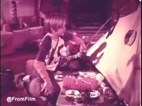 The still from the 1970s Puff's Tissues commercial features a young boy in a playful indoor campsite setting. He sits beside a makeshift tent, surrounded by snacks and bowls. The color palette has a soft, vintage feel, characteristic of 16mm film. It captures the innocent whimsy of childhood fun, emphasizing the durability and usability of Puff's Tissues in a relatable, family-oriented scenario.