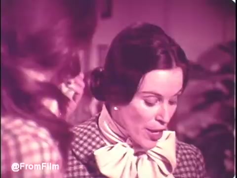 This 16mm still from a 1970s Puff's Tissues commercial features two women in a domestic setting. One woman is dressed in a checkered outfit with a large bow at her neck, while the other appears to be giving her attention. The color tone suggests a vintage look, capturing the era's aesthetic. The tagline highlights the availability of Puff's Tissues in blue and green, emphasizing a playful approach to advertising. Follow us on Twitter @FromFilm for more film-related content.