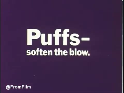 The still features a simple yet striking graphic design typical of 1970s commercials. The deep purple background contrasts with the bold white text that reads 'Puffs - soften the blow.' This tagline emphasizes the softness and comfort of Puffs tissues, suggesting a gentle experience. The visual aesthetic reflects the era's advertising style, aiming to attract attention and convey the product's benefits succinctly.