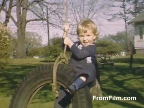The still features a joyful child swinging on a tire swing in a vibrant backyard, showcasing the cheerful atmosphere of post-war life in Holland, Michigan. The warm, rich colors typical of Kodachrome film capture the essence of outdoor play. This scene, predating the famous Tulip Time Festival, offers a nostalgic glimpse into everyday moments before the celebration of tulips began.