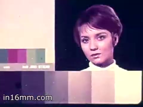 The still shows a woman with short, styled hair, looking directly at the camera. She appears to be in a video production setting, possibly a rehearsal or test shot. To the left are color swatches, likely used for adjusting lighting or film quality, while the background is a simple gradient. The overall aesthetic reflects the 1960s style, combining a clean, modern look with an emphasis on color.