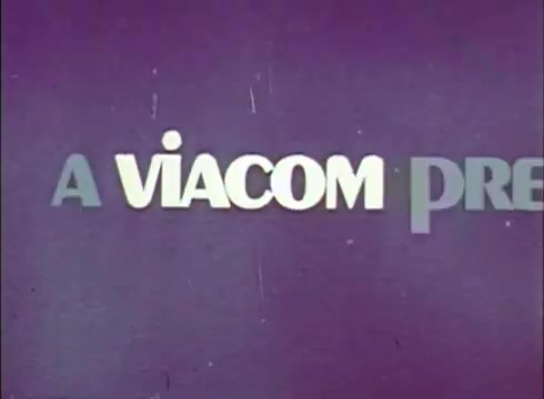 The still displays a text overlay that reads 'A VIACOM PRE' against a solid purple background. The text is stylized, with varying font weights and sizes, suggesting a classic broadcast introduction. There are visible scratches and grain typical of a 16mm film print, indicating some wear. An out-of-focus object appears in the lower left-hand corner, possibly a lab defect or artifact from the print.