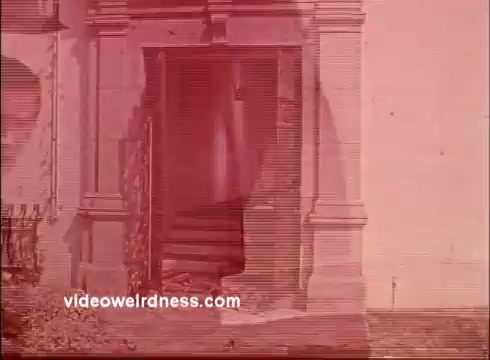 The still appears to depict a doorway, likely with historical or architectural significance, set against a reddish tint typical of some aged 16mm prints. There may be signs of wear or distortion, characteristic of vintage film. The overall composition suggests a contemplative or inviting atmosphere, aligning with the themes of unity and spirituality conveyed by Joe Campanella in the context of the Unity Church commercials.