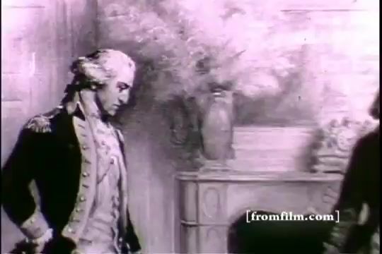 The still from 'Great Moments in History - Army Recruiting' depicts a historical figure in a military uniform, emphasizing a reflective or contemplative expression. The background features decorative elements like a vase, contributing to a period setting. The monochrome tone suggests an older film style, typical of 16mm prints. The figure appears to be engaged in a thoughtful moment, likely related to themes of leadership or recruitment in a historical context.