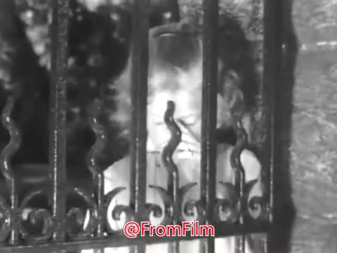 The still from 'PSA From Guideposts Magazine - 1968' features a young girl, around eight years old, standing behind a wrought-iron fence. Her expression conveys a sense of loneliness and sadness, emphasizing her feelings of isolation as she is described as painfully shy and shunned by peers. The context highlights her struggles within the orphanage setting, underscoring the challenges faced by children in such environments during that time.