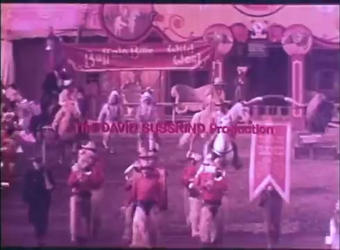 The still from the trailer of 'Buffalo Bill and the Indians' showcases a vibrant scene featuring a parade or performance. Groups of individuals dressed in historical Western attire are mounted on horses, accompanied by banners and a colorful backdrop of tents. The production credits prominently display 'THE DAVID SUSSKIND Production' in bold red text, adding to the theatrical feel. The overall aesthetic appears lively and celebratory, indicative of Western genre filmmaking.