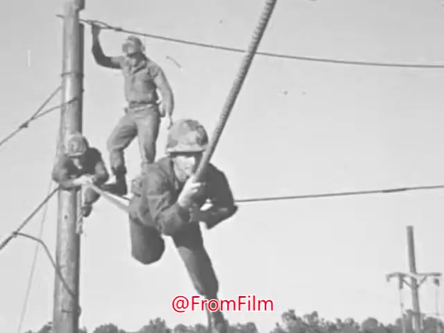The still from the 'US Marines recruiting PSA' shows three Marines engaged in physical training. One Marine is climbing a rope, demonstrating strength and agility, while two others can be seen in the background, possibly navigating the obstacle course as well. The setting appears to be outdoors, likely part of a training facility, showcasing the rigorous and disciplined environment of Marine training during the late 1960s, coinciding with the Vietnam War era. The emphasis on physical fitness underscores the message of leadership and personal development conveyed in the accompanying voice-over.