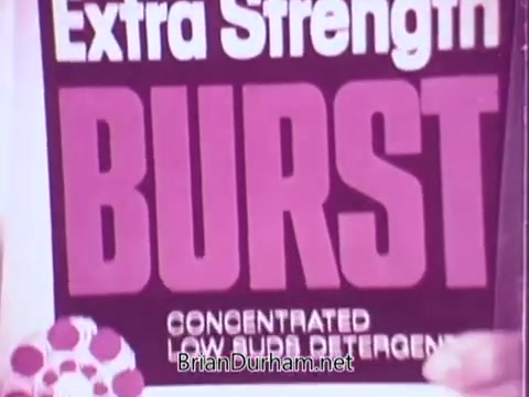 The still features a bottle of 'Colgate Burst' low suds laundry detergent. The label prominently displays the words 'Extra Strength' and 'BURST' in bold, vibrant lettering. The design emphasizes the product's concentrated formula, highlighting its low sudsing properties. The background has a simple design, focusing attention on the product's branding.
