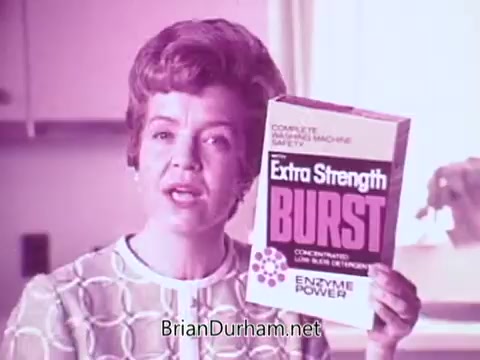 The still features a woman holding a box of 'Extra Strength Burst' low suds laundry detergent. She is likely promoting the product, emphasizing its effectiveness for washing. The setting appears to be a kitchen, and the color palette has a vintage aesthetic, typical of mid-20th century advertisements. The focus is on the product and the woman's engagement with the audience.