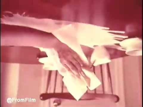 The 16mm still from 'Bounty Commercial Threaded Backwards...' features a close-up of a person's hands delicately handling paper towels. The scene appears to be reversed, adding an unusual visual twist typical of experimental editing. The colors are likely muted or faded, characteristic of older film prints. The placement of objects like a chair hints at a domestic setting, emphasizing the focus on the paper towels. Overall, the still conveys an intriguing glimpse into the creative manipulation of commercial footage.