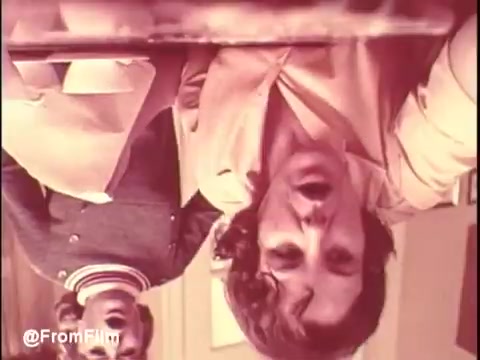 The still from 'Bounty Commercial Threaded Backwards...' features two figures. One is prominently shown with a facial expression suggesting intensity or surprise, likely speaking or reacting to something off-screen. The other figure, dressed in a jacket with stripes, is positioned in the background but also catches the viewer's attention. The overall mood likely reflects the commercial's intended message or theme, though the backward splicing adds a surreal twist. The colors appear soft, typical of 16mm film, contributing to a vintage aesthetic.