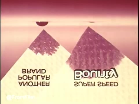 The still features a stylized visual representation related to a Bounty commercial, presented in reverse. It showcases two pyramid-like shapes prominently displayed, decorated with textured patterns. The text, creatively inverted, reads 'Bounty' alongside phrases suggesting speed and brand authenticity. The color palette is soft with a gradient background, likely contributing to a playful and inviting aesthetic. The unusual presentation adds a layer of intrigue, hinting at the unconventional approach of reversing the footage for artistic effect.