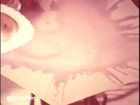 The still from 'Bounty Commercial Threaded Backwards' features a tabletop scene that's likely part of a commercial. It appears to show a colorful liquid, possibly a spill or paint, splattering across a surface, creating an abstract, dynamic effect. There's also a plate, possibly with food, indicating a household or kitchen setting. The reversed nature of the clip may add an intriguing visual twist, emphasizing the fluid motion. The image has a vintage aesthetic, typical of 16mm prints.