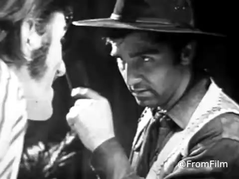The still from the 'Jello Commercial - 1970's' features two characters engaged in an intense interaction, likely conveying humor or a playful storyline. The image is presented in black and white, emphasizing expressions and details despite the faded quality typical of a 16mm print. One character leans in closely, possibly making a point or asking a question, while the other listens intently, creating a moment of tension or intrigue. The overall composition captures the whimsical and often eccentric nature of commercials from that era.    for more content!