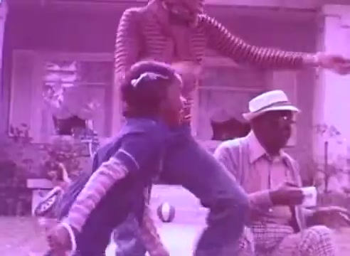 The still appears to depict a joyful outdoor scene featuring a child playing, with an adult watching nearby. The color scheme has a pronounced purple tint, giving the image a stylized look. The setting seems casual and familial, suggesting themes of health and togetherness, aligning with the message of taking blood pressure medication for loved ones.