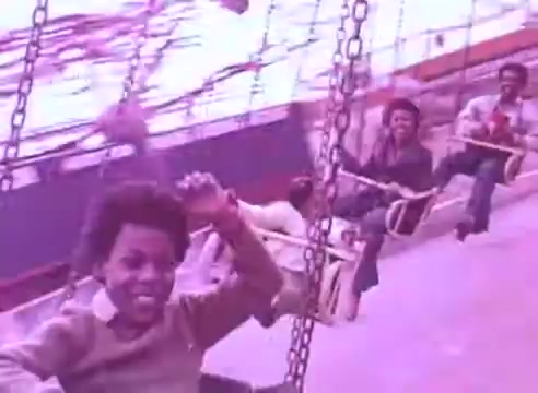 The still depicts a vibrant scene from the film 'Do it for them' - take your blood pressure medication 3. It features several individuals on a swing ride, conveying a sense of joy and carefree fun. The image has a warm, nostalgic tone, enhanced by the pinkish hue, suggesting themes of happiness and community, possibly linked to the importance of taking care of one's health for loved ones.