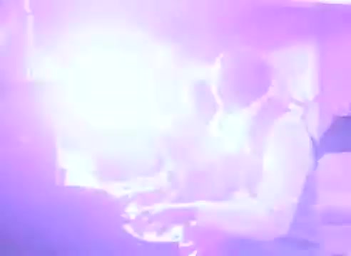 The still from 'Do it for them - take your blood pressure medication 3' features a blurred, luminous scene dominated by bright purple and white light. The focus seems to be on a person, possibly playing an instrument, though the details are obscured by the intense lighting. The ethereal glow creates a dynamic and energetic atmosphere, suggesting a moment of urgency or excitement related to the theme of health and medication.