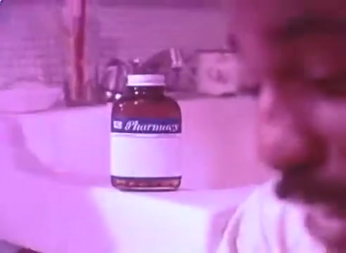The still from 'Do it for them' - take your blood pressure medication 3 features a close-up of a man, with a focus on a prominent prescription bottle labeled 'Pharmacy' in the background. The color palette is soft, with a pink hue, suggesting a warm and inviting atmosphere. The context emphasizes the importance of taking blood pressure medication for the sake of loved ones.