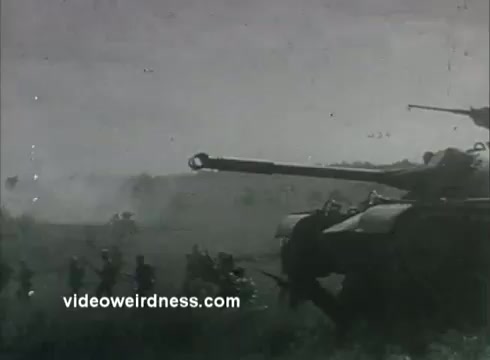 The still shows a tank on a battlefield with soldiers advancing in the background. The scene is likely intended to evoke a sense of patriotism and enlistment, characteristic of 1950s Army recruiting PSAs, reflecting military strength and readiness. The monochrome film adds to the historical context.